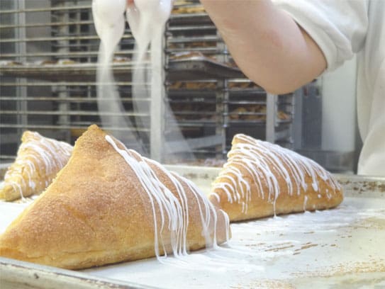 a chef is drizzling icing on a pastry