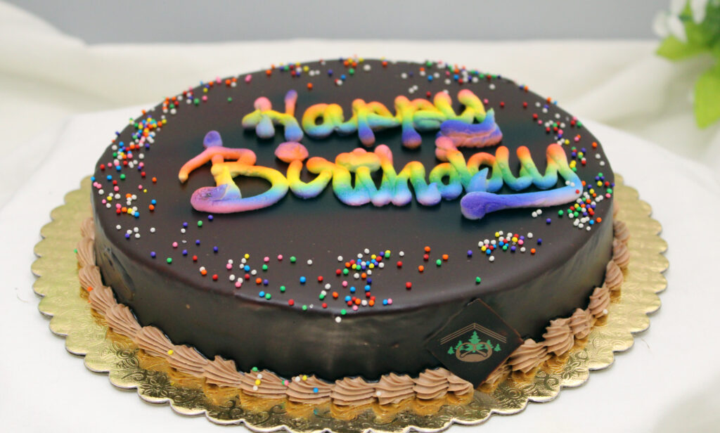 Dense Brownie-like cake with a thin layer of Chocolate Truffle Filling and topped with Chocolate Ganache, with rainbow writing!